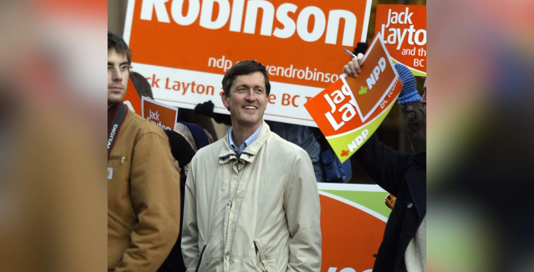 Svend Robinson at a Pride event with campaign signs in the background.