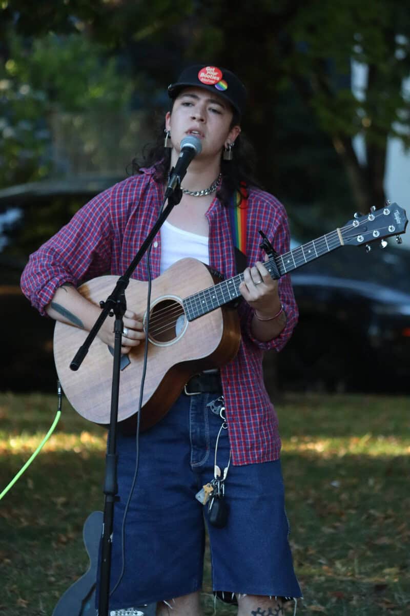 Young person singing and playing guitar at outdoor event.