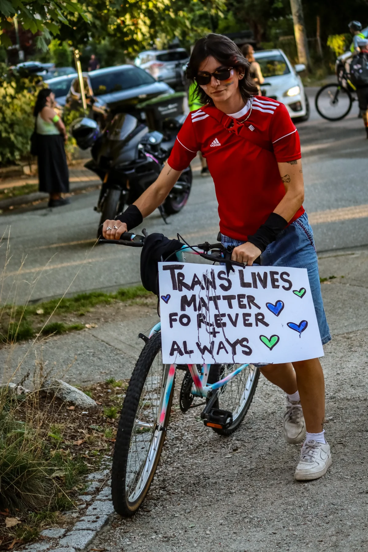 Woman with a bicycle holding a sign supporting trans rights at a park.