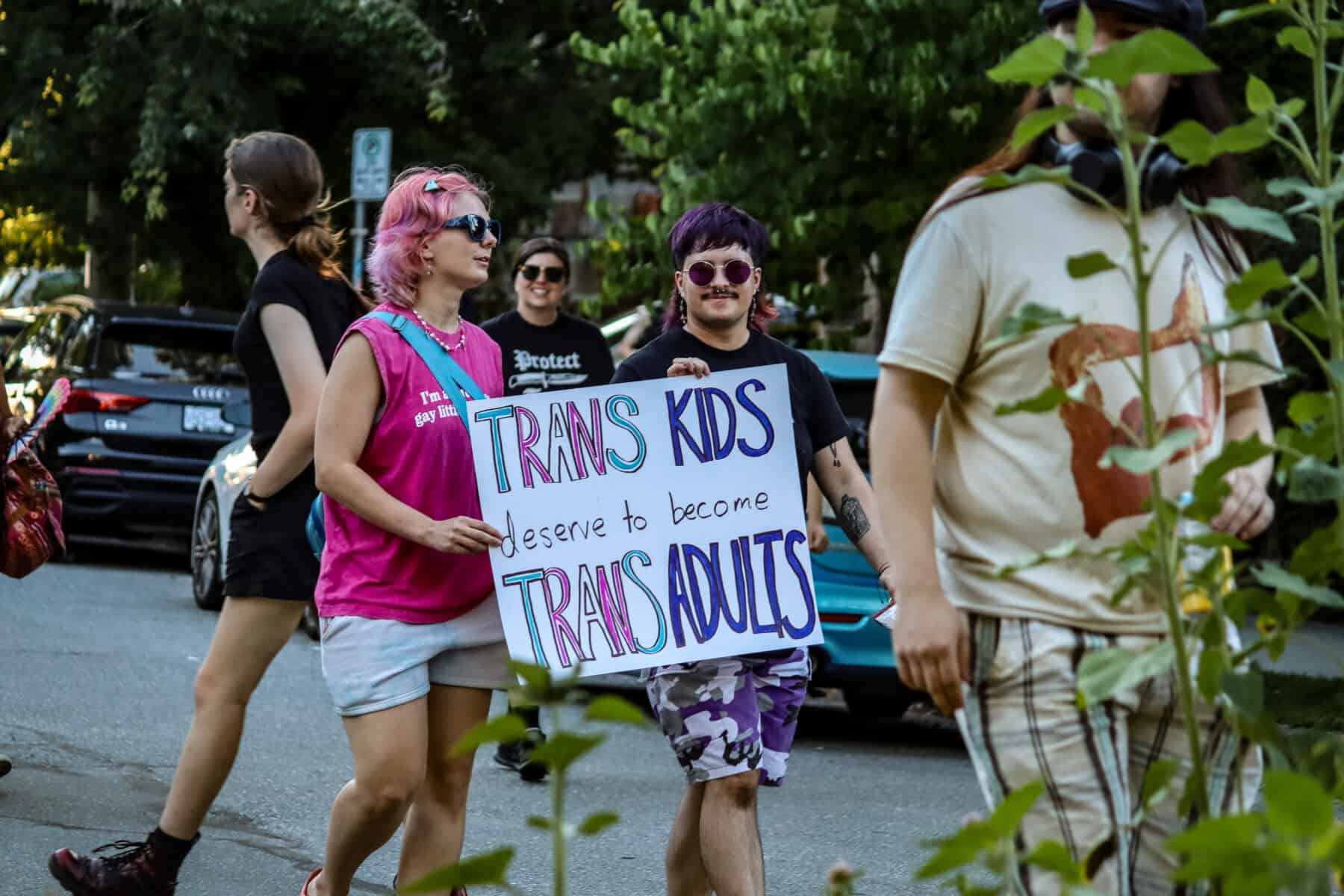 Trans march participants holding a sign advocating for trans kids and adults.