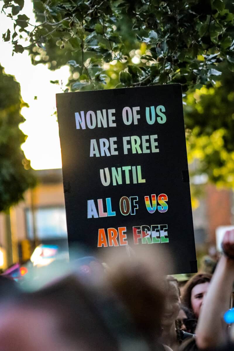 Protest sign reading 'None of us are free until all of us are free' at Vancouver Trans March.