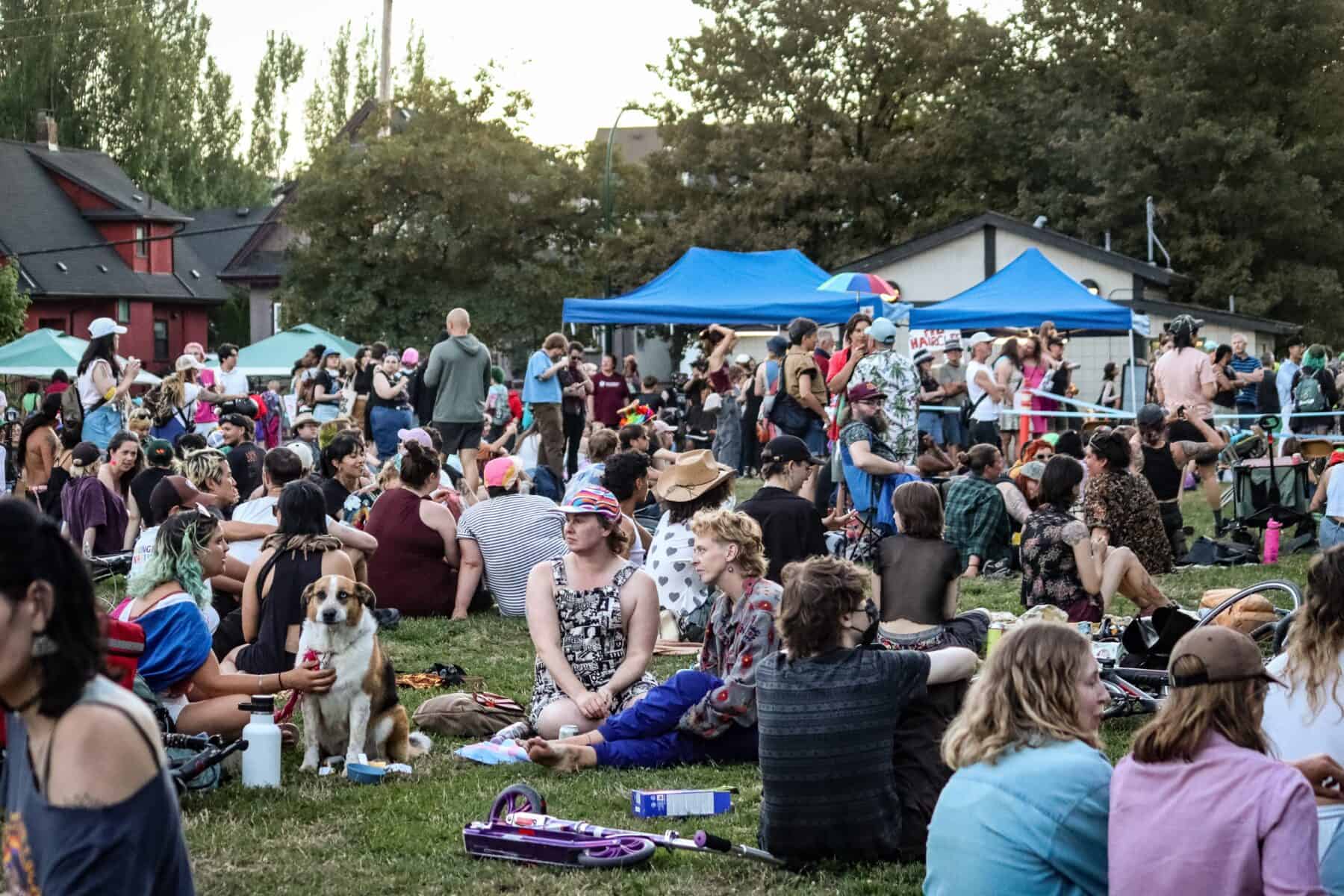 Large crowd gathers at Vancouver Trans March outdoor event with tents and trees.