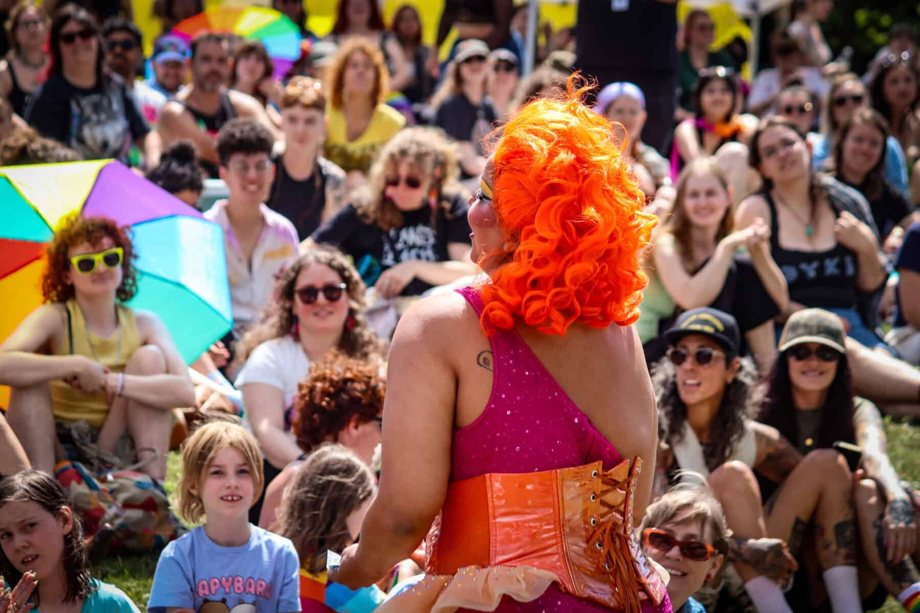 Performer with bright orange hair entertains crowd at outdoor event.