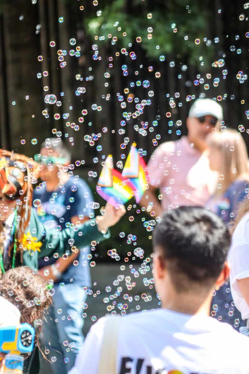 LGBTQ+ pride parade with bubbles and rainbow flags in a park setting.