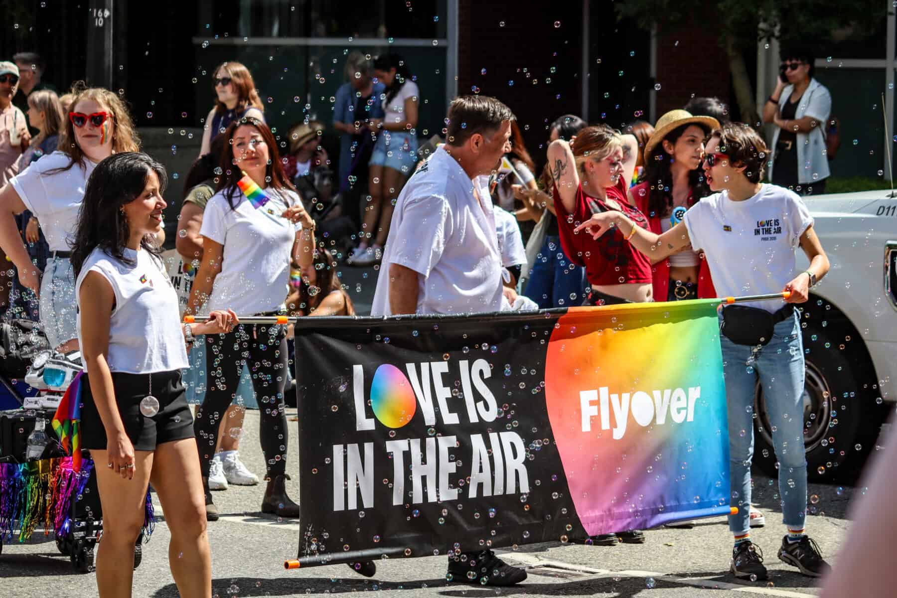 LGBTQ+ pride parade with diverse participants holding a rainbow banner.