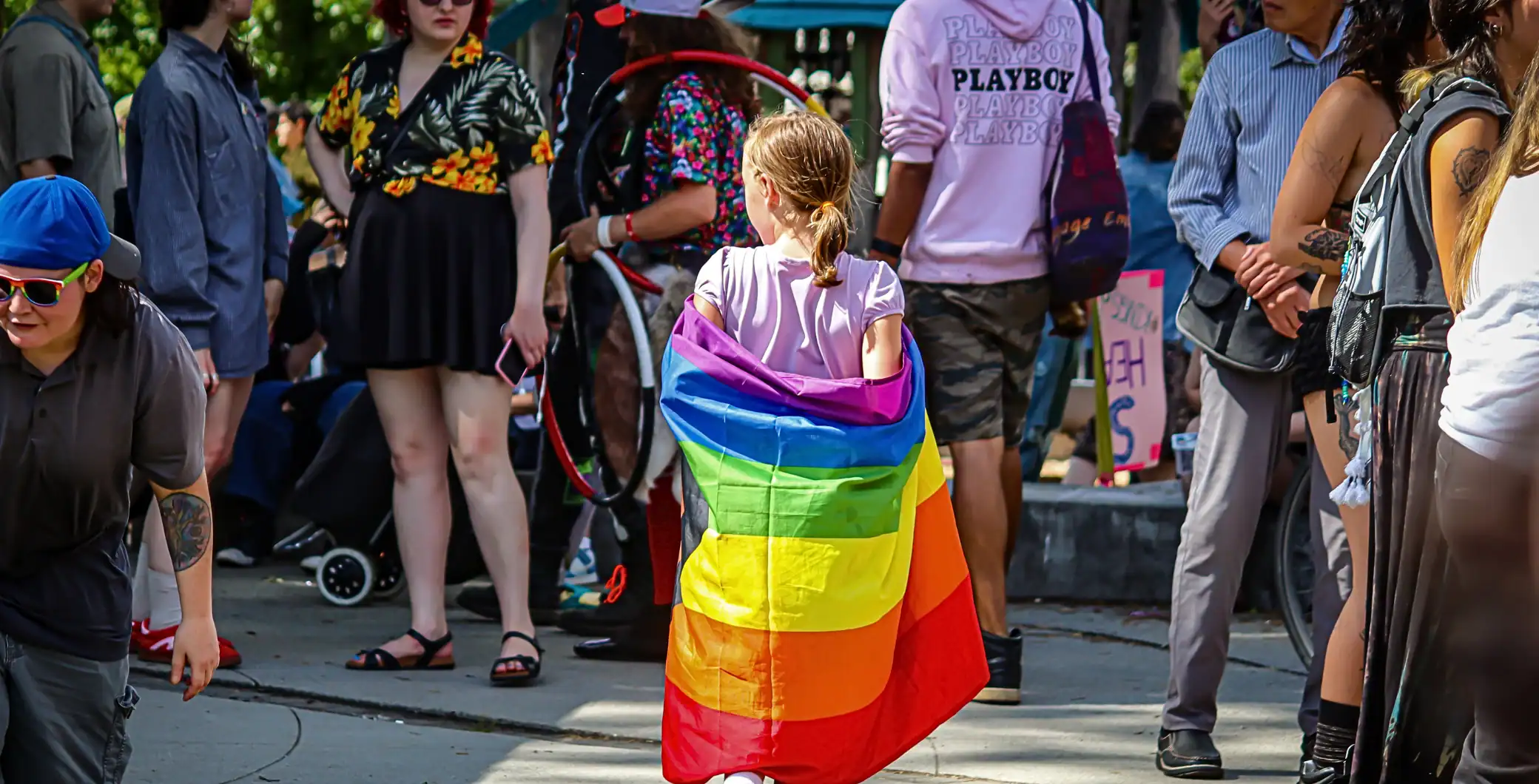 Young woman with rainbow flag at pride march, diverse crowd in background.