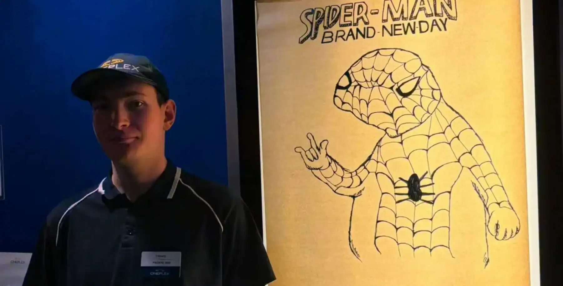 Young man in black cap standing next to Spider-Man poster at Now Canada event.
