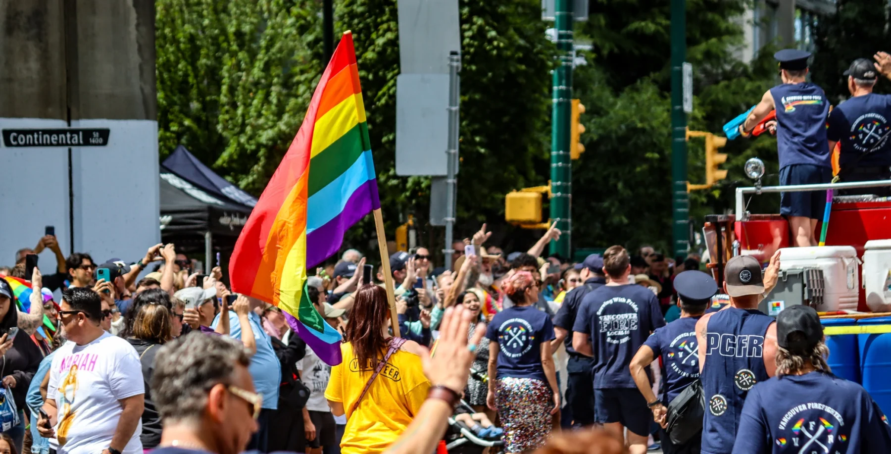 LGBTQ+ pride parade with rainbow flag and diverse crowd in downtown Toronto.