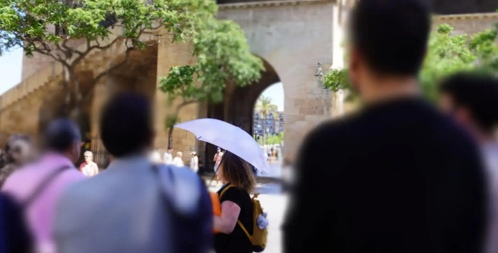 People walking under an umbrella near historic stone architecture in a city.