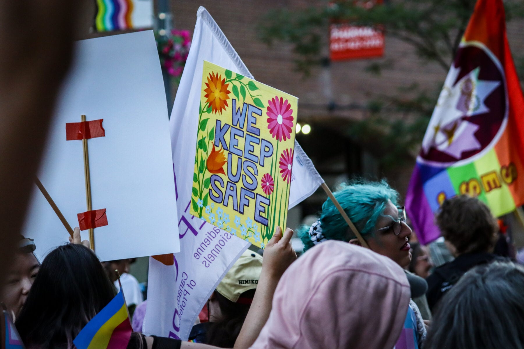 Queer and trans march participants hold signs and flags in Ottawa.