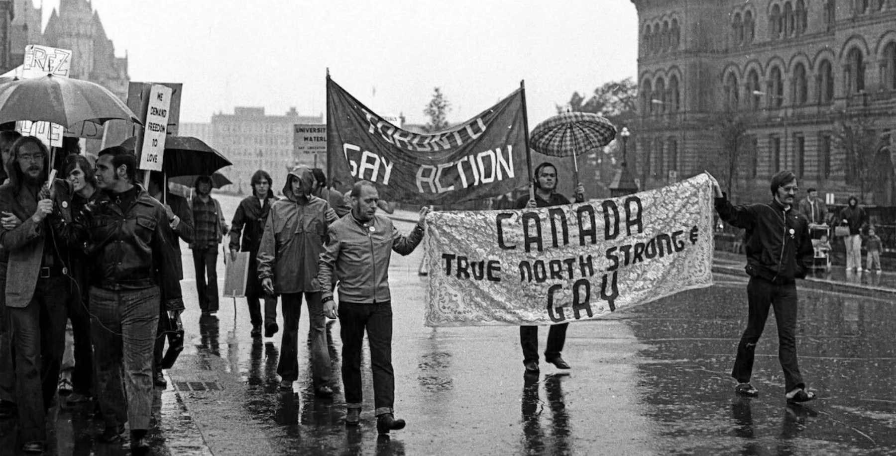 LGBTQ+ pride parade with protest banners in rainy weather in Ottawa.